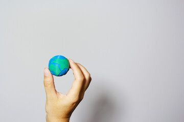 Single hand forming protective cup around miniature Earth globe against neutral background, symbolizing environmental care and global protection. Earth day concept. Responsible business. 
