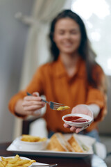 Smiling woman enjoying healthy eating with fries and dipping sauce, dressed in a stylish orange...