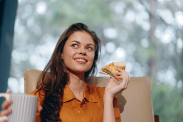 Smiling woman enjoying a healthy snack while sitting in a bright room with nature background,...