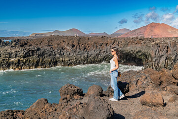 A young brunette woman enjoys the dramatic volcanic cliffs and ocean views at Los Hervideros,...