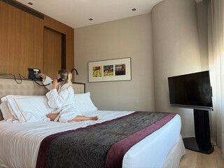 Woman in white hotel bathrobe talking on a landline phone while sitting on the bed. Possibly making...