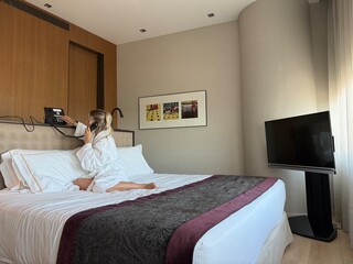 Woman in white hotel bathrobe talking on a landline phone while sitting on the bed. Possibly making...