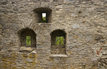 Small arched windows in the stone wall of the castle. Arched windows of the walls. View of the surroundings, peephole for defending archers. Texture of the stone wall. Exploring Czech monuments.