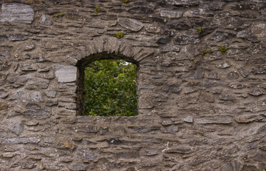 Small arched windows in the stone wall of the castle. Arched windows of the walls. View of the surroundings, peephole for defending archers. Texture of the stone wall. Exploring Czech monuments.