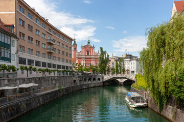A picturesque view of the Ljubljanica River flowing through the charming city center of Ljubljana, Slovenia, under a bright, partly cloudy sky