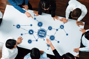 A diverse group of professionals actively engages in discussion around a table featuring graphic...