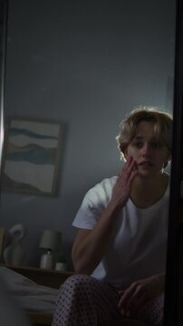Vulnerable young woman looks at reflection in mirror on bed