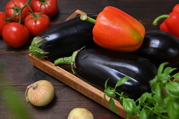 wooden box with fresh summer vegetables, eggplants, sweet peppers and herbs