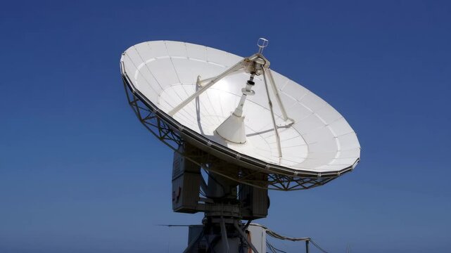 A large satellite dish rotates to establish connections high above the ground. The equipment is stationed in a remote area, against a vibrant blue sky, showcasing advanced communication technology