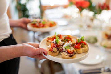 Close-up of a person holding a plate with assorted bruschetta topped with tomatoes, greens, and...