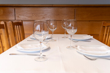 Empty wine glasses and plates are set on a white tablecloth, ready for diners in a restaurant with...