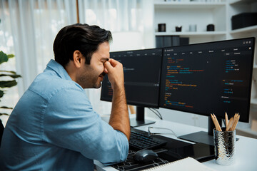 Stressful IT developer having eyestrain to overwork in data software development on two pc screen,...