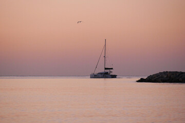 A breathtaking sunset over the calm sea with a sailboat on the horizon. Warm orange and golden...