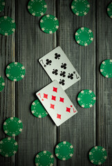 Two playing cards featuring the number two are placed amidst green poker chips on a wooden surface, showcasing an engaging card game atmosphere at night