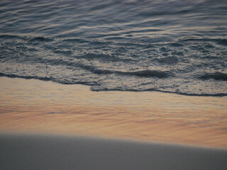 Gentle ocean waves lapping against the shore with wet sand. A serene coastal scene during golden hour. Background theme related to relaxation, mindfulness, travel, nature, and wellness