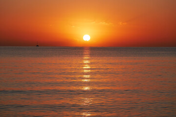 Vivid sunset over the sea with a glowing sun and golden reflection on the calm water. Peaceful and...