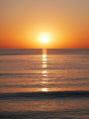 Vivid sunset over the sea with a glowing sun and golden reflection on the calm water. Peaceful and captivating atmosphere. Nature background, relaxation concept, travel theme and inspirational visual