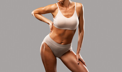 A slender swarthy woman in beige underwear on a dark background. Healthy lifestyle, sport and diet.