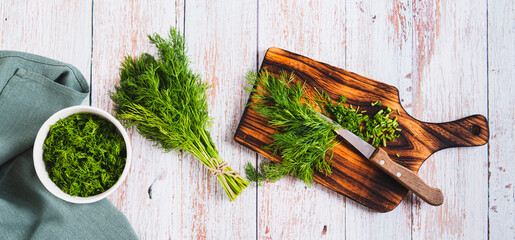 Chopped fresh dill and knife on cutting board on table top view web banner