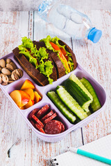 Lunchbox with sandwich, chorizo, cucumber and peach, bottle of water on table vertical view