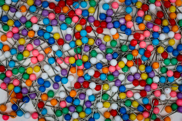 Many bright ball head pins scattered on a white background.