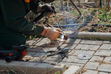 A man works with a welding machine. Sparks from welding. Joining metal parts using a welding machine. The workflow of an electric welder. The welding process in the courtyard of a private house.