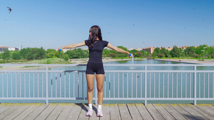 Fit woman working out with weights on a wooden pier near a lake