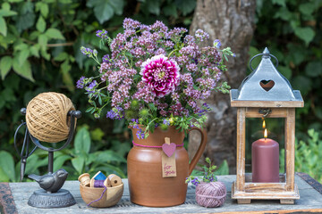 Garten-Arrangement mit Blumenstrauß mit pink Dahlie und Feldthymian im rustikalen Krug und Laterne
