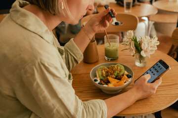 Middle-aged woman scrolls her social media feed on mobile phone in a cozy cafe. Small business....