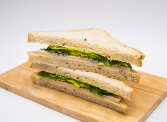 Classic Chicken Caesar Sandwich with Fresh Lettuce on Seeded Bread on wooden board side view of fast food on white background