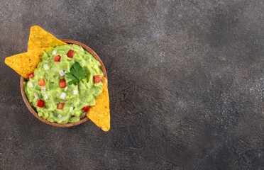 Mexican appetizer guacamole dip with ripe hass avocado, tomatoes, jalapenos, crispy tortilla chips. Top view. Copy space