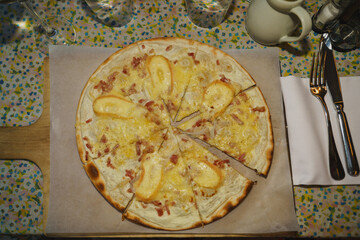 A traditional Alsatian flammkuchen with goat cheese, bacon, and onions is served on a wooden board—perfect for culinary, regional, or food concept photography