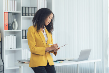 Confident Professional at Work: A determined businesswoman in a vibrant yellow jacket, meticulously...
