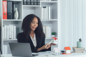 Real estate agent in Office: A real estate agent sits in her office, presenting a model home to a...