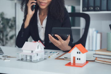 Real Estate Negotiation: A diligent realtor on a call, surrounded by miniature house models,...