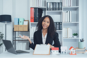 Smiling Real Estate Agent at Desk: A confident woman, showcasing a welcoming gesture as a real...