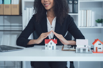 House Protection by Businesswoman: A confident professional safeguards miniature house models,...