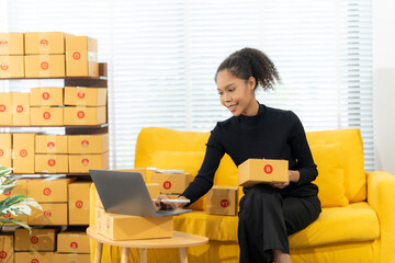 Businesswoman Manages Online Orders: A happy businesswoman on a vibrant yellow couch manages online...
