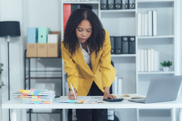 Professional in Office: A focused businesswoman diligently reviews documents and calculates data at...