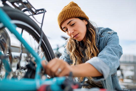 Woman repairs e-bike with DIY toolkit at outdoor bike rack on a sunny day