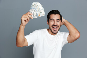 Happy smiling man in white t-shirt holding cash in hand, looking at the camera, isolated on plain...