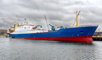 huge stern trawler is moored in the herring harbour in IJmuiden Netherlands under a cloudy sky.