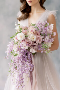 Bride holding a cascading bouquet of pastel roses, wisteria, and delicate blooms in soft pink, lavender, and ivory
