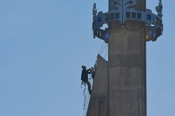 A skilled worker fixes the tower of a modern church. A roofer works on the tower of a modern building. The concept of working at height and safety at work