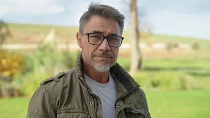  Portrait of confident middle aged man wearing glasses outdoor. Farmer, landowner standing on ranch with proud look. Rural life and agriculture. Mature male with gray hair in military coat. © nyul