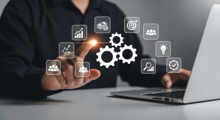A person interacting with digital icons and gears on a laptop screen in a business setting