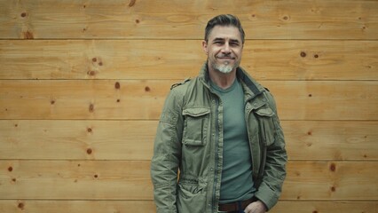 Confident happy man smiling next to rustic wooden wall. Mid adult, middle aged mature male in 50s...