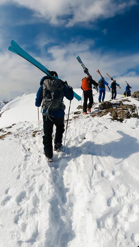 Skiers hiking up a snowy mountain ridge with skis on their shoulders under a clear blue sky. Adventure, teamwork, and alpine freedom.