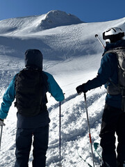 Two skiers admire a pristine mountain slope carved with fresh tracks under a clear blue sky. The thrill of untouched powder and alpine freedom.
