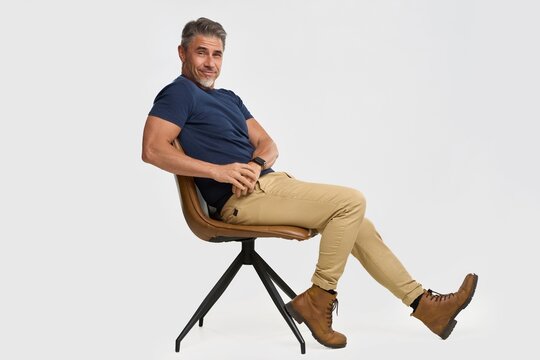 Confident middle-aged man in casual clothes sitting relaxed on chair, posing on white background. Happy mid adult, mature male smiling. Full length portrait photo.